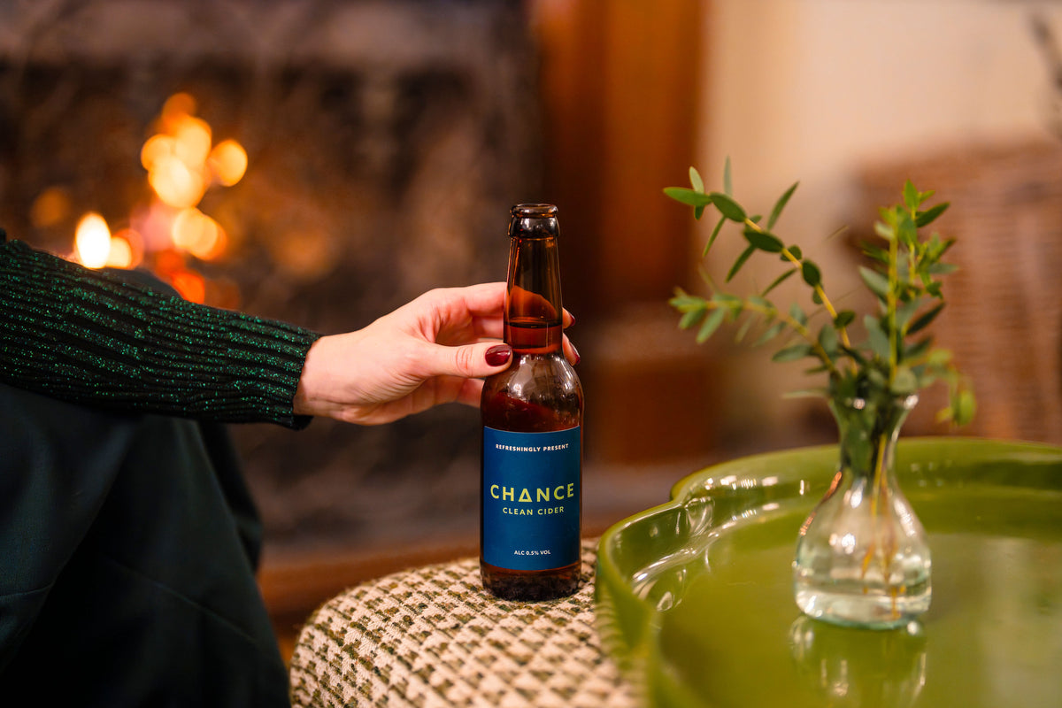 Person holding a bottle of 'Chance' cider in front of a fireplace